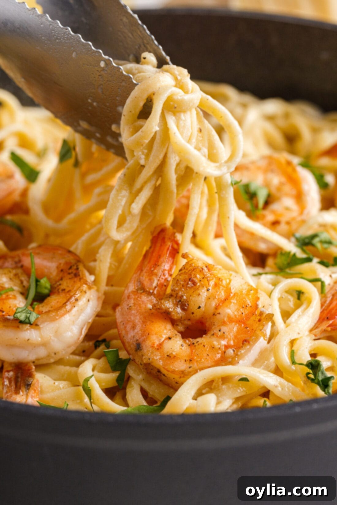 Zesty Garlic Shrimp Pasta 3 tongs lifting Shrimp Pasta from a skillet, showcasing the perfectly coated noodles and shrimp.
