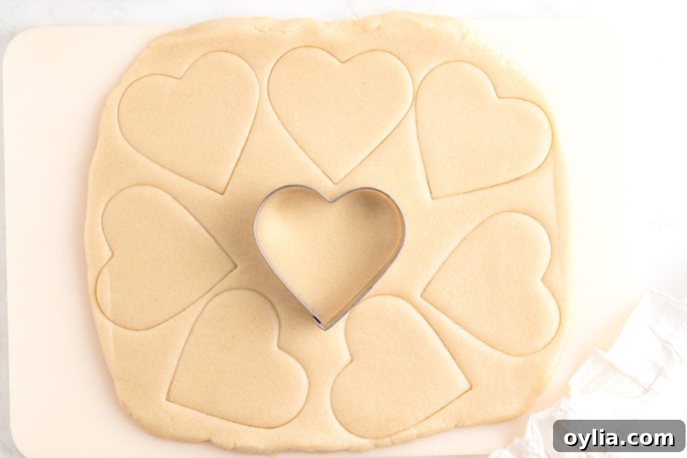 Heart-shaped cookie cutter pressing into rolled-out sugar cookie dough, ready for baking.