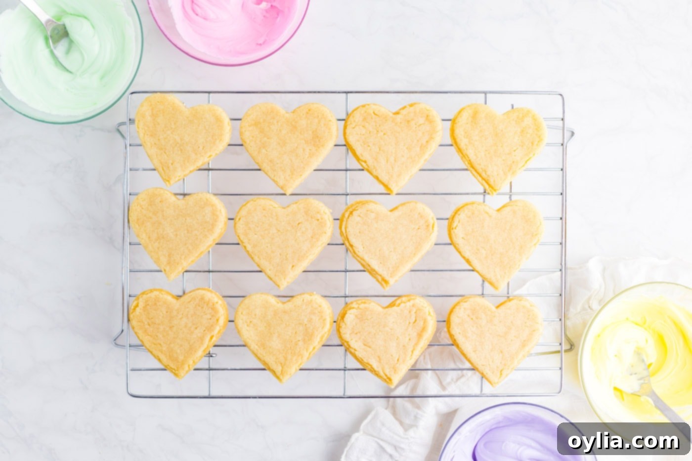 Freshly baked heart-shaped sugar cookies cooling on a wire rack, essential before frosting for best results.