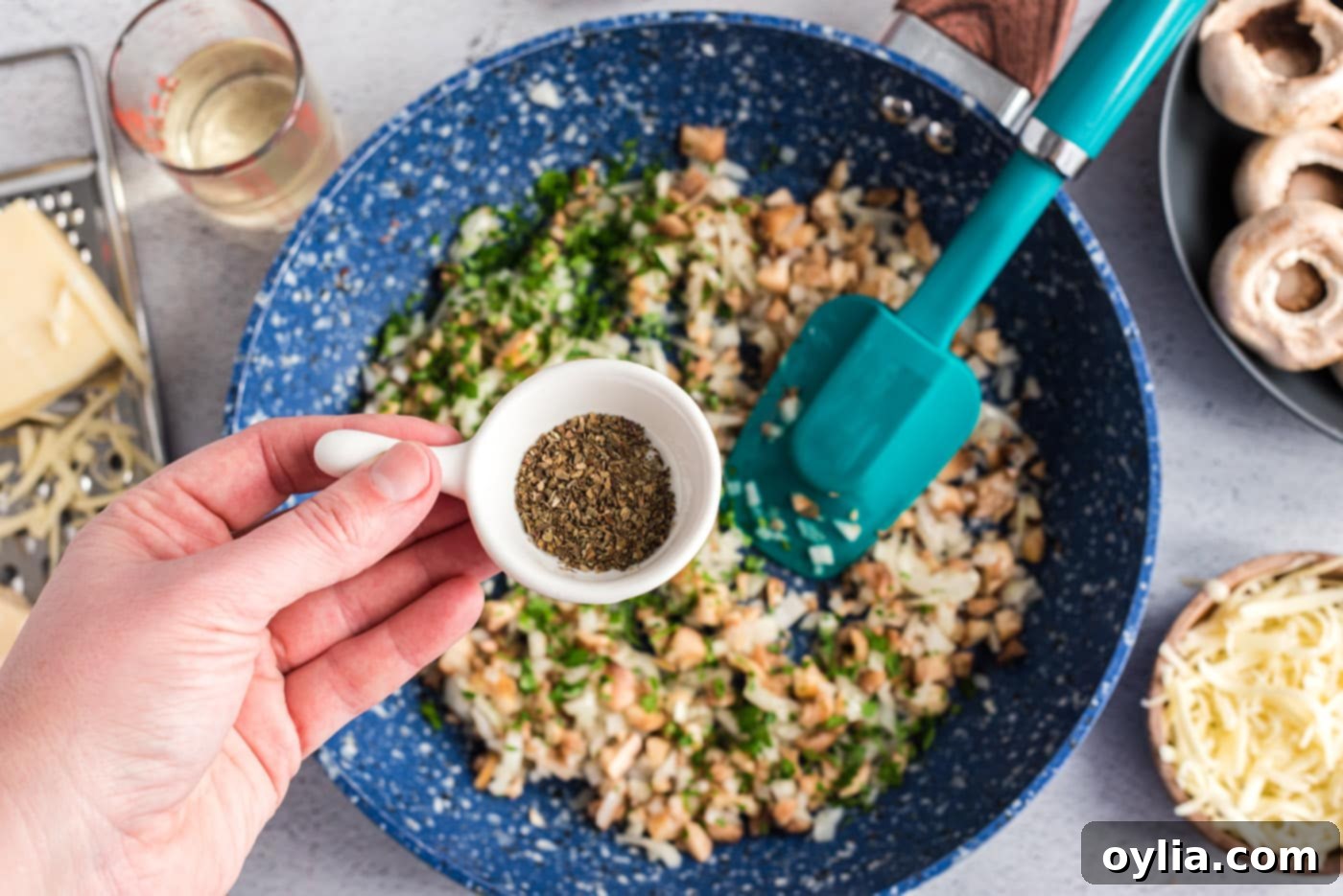 Adding dried basil to the sautéed onion and mushroom stem mixture in a skillet, preparing the filling for stuffed mushrooms.