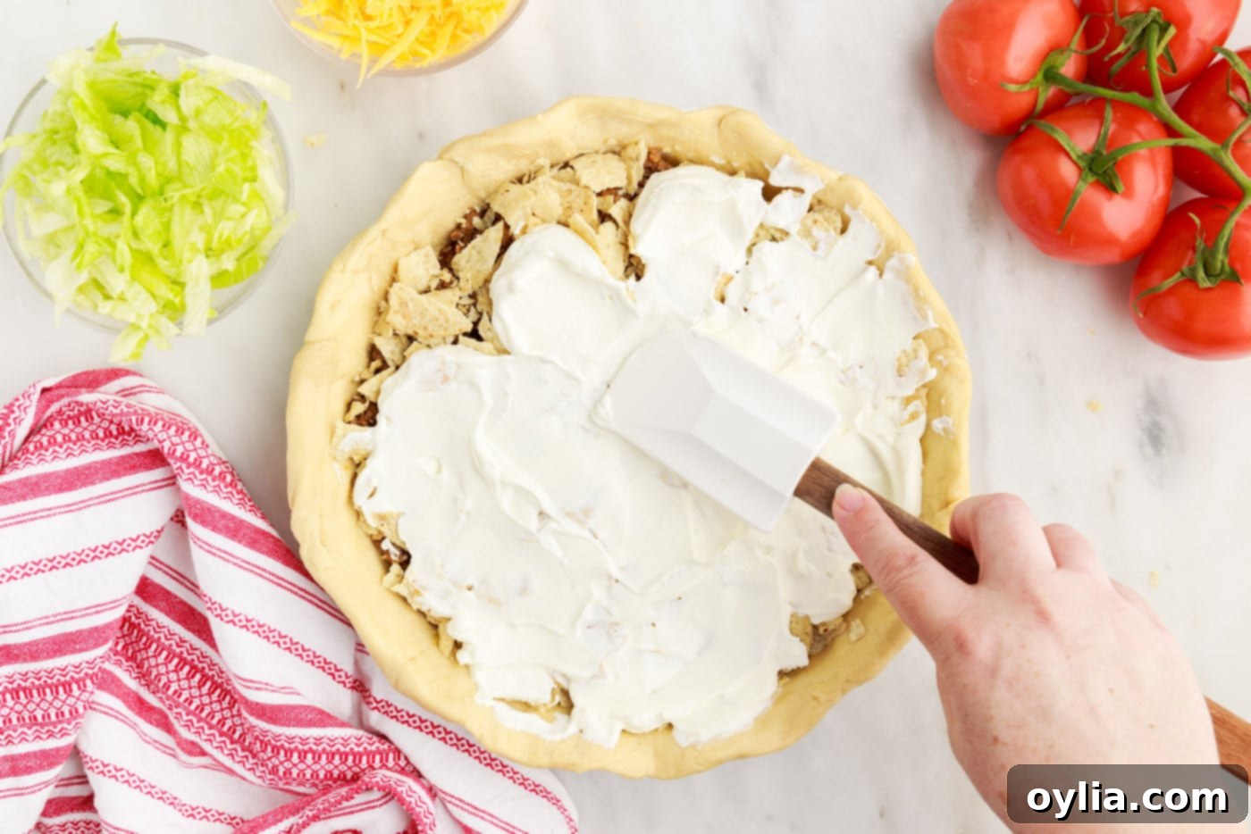 a spatula smoothly spreading sour cream over the taco pie layers