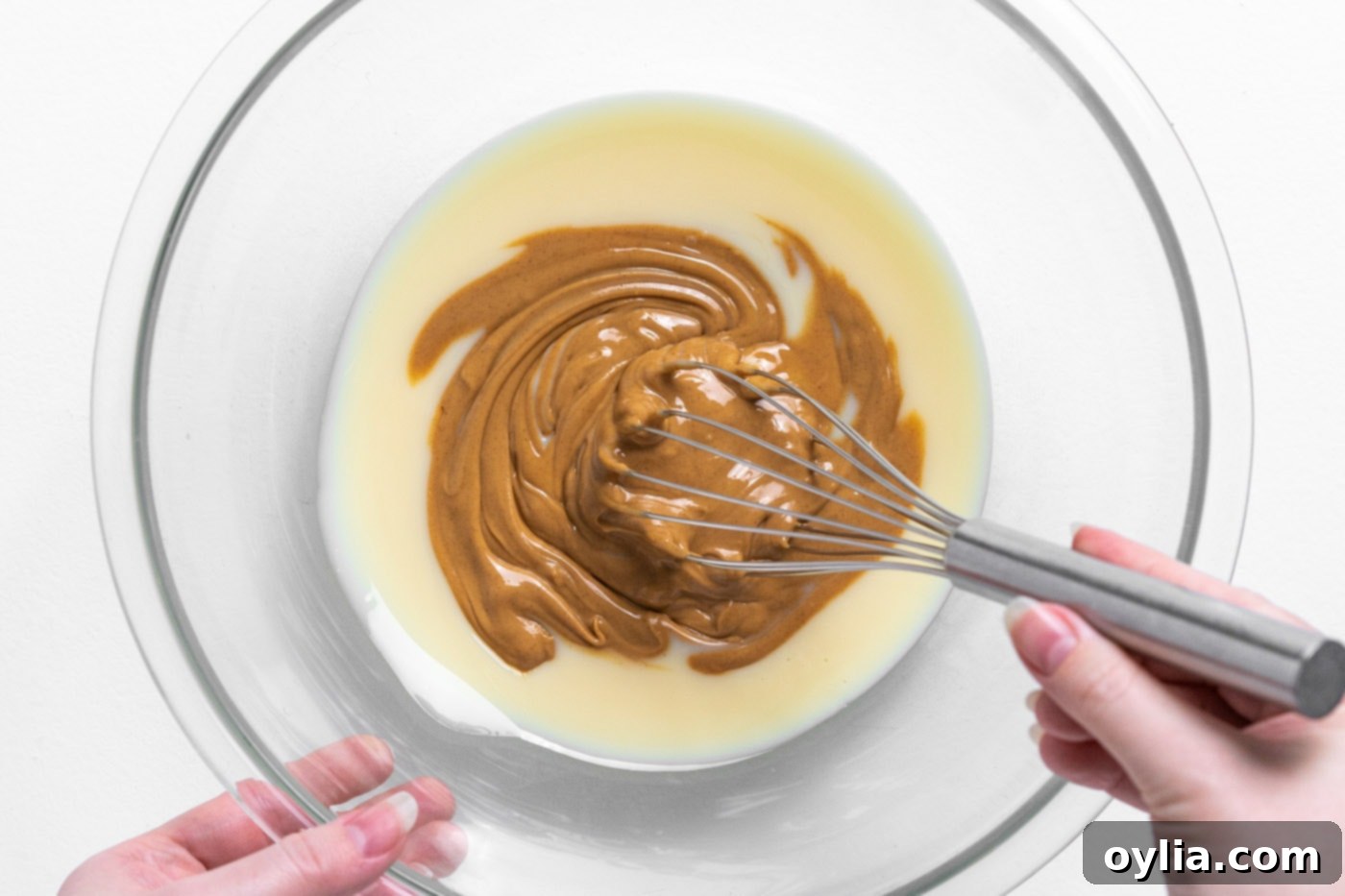 A close-up image showing sweetened condensed milk and peanut butter being whisked together in a bowl until smooth.