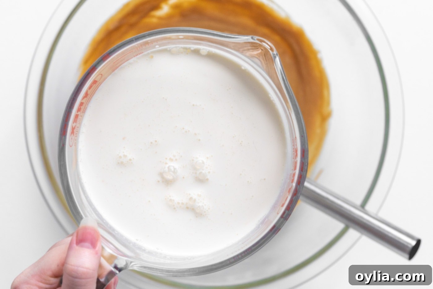 Pouring the heavy whipping cream, half and half, and vanilla mixture over the whisked peanut butter and condensed milk mixture in a bowl.