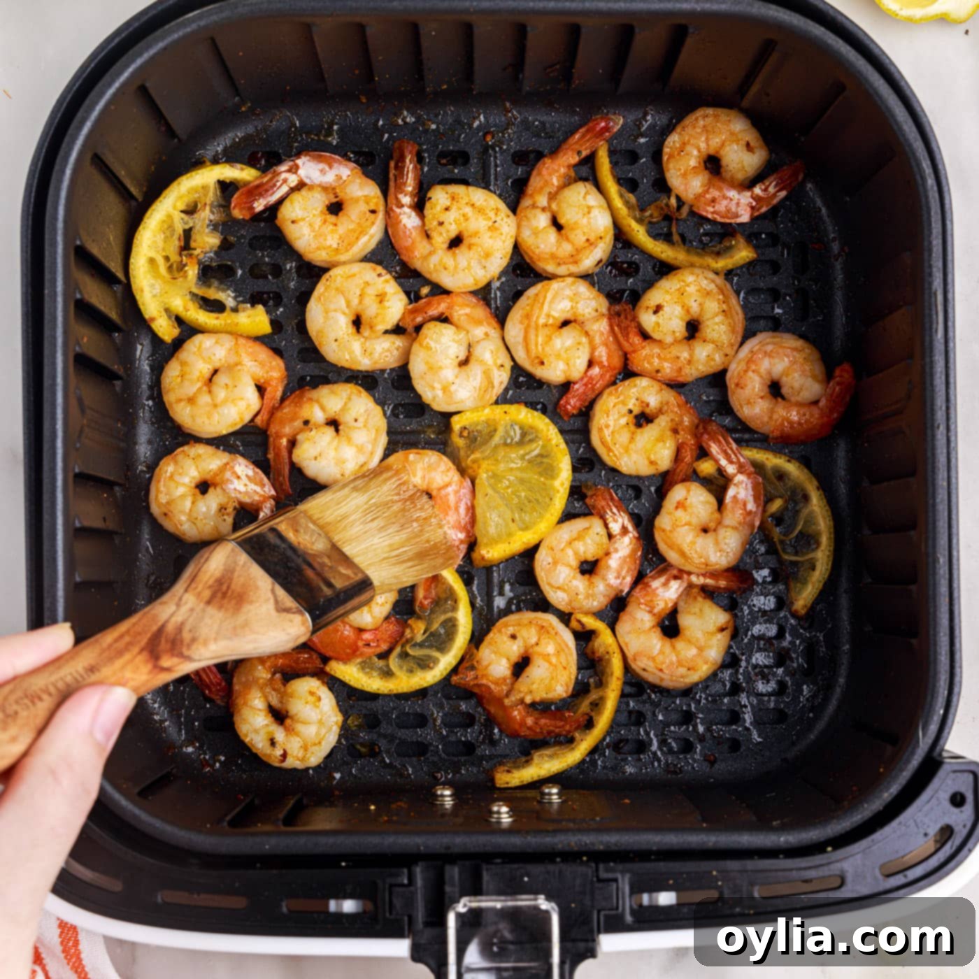 Brushing melted butter onto cooked shrimp in an air fryer basket.