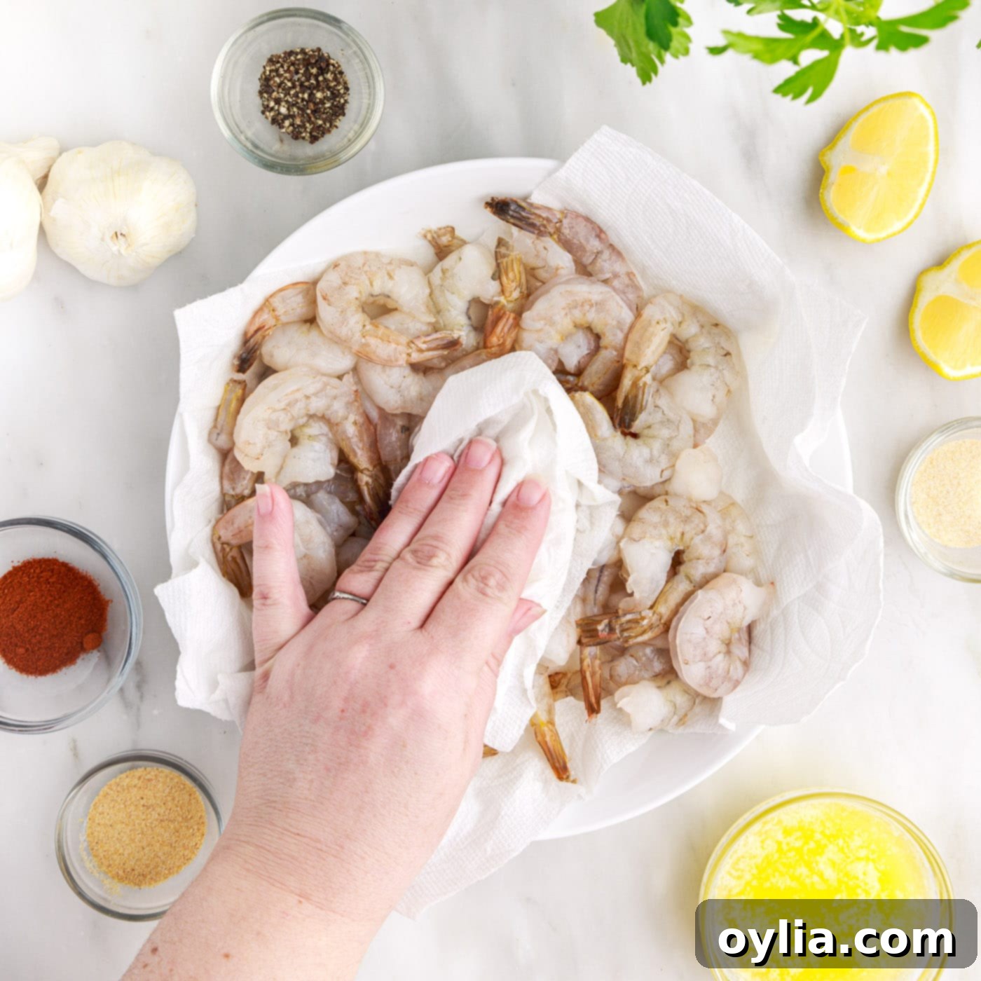 Patting raw shrimp dry with a paper towel on a cutting board.