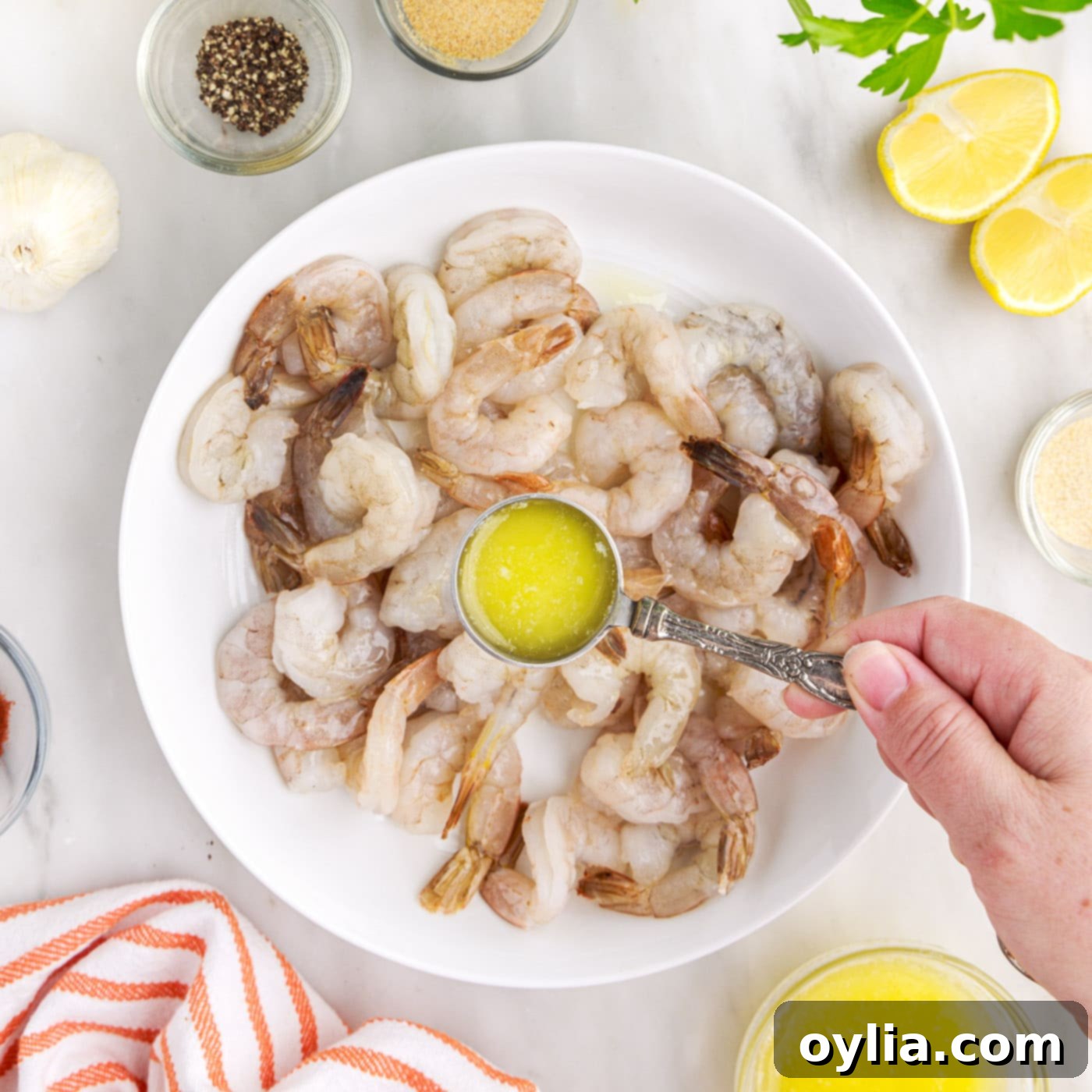 Pouring melted butter over raw shrimp in a mixing bowl.