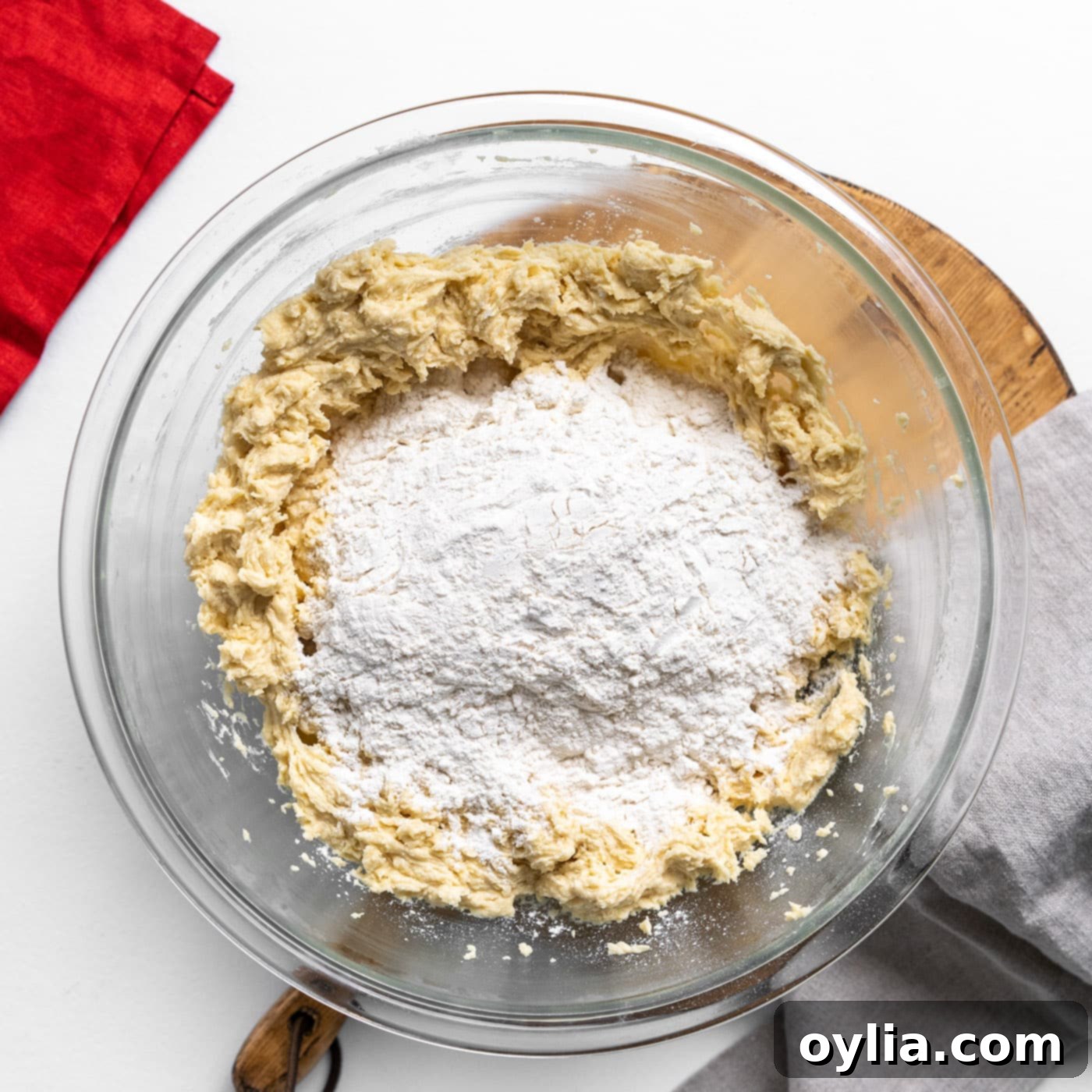 Dry ingredients, including flour and oats, added on top of the wet cookie dough in a mixing bowl