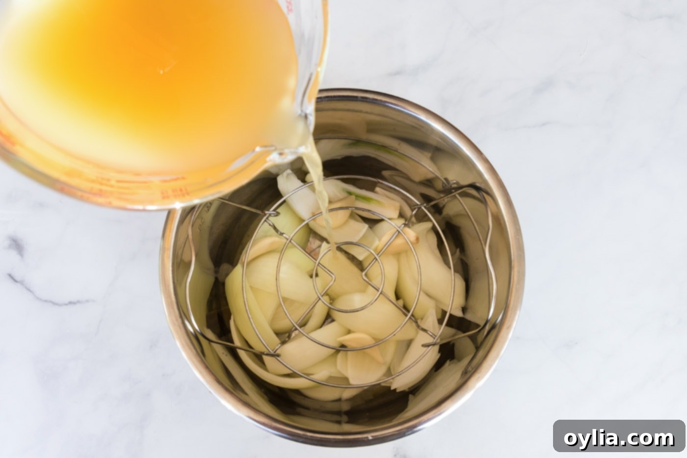 Broth being poured over onion wedges and garlic cloves in the Instant Pot