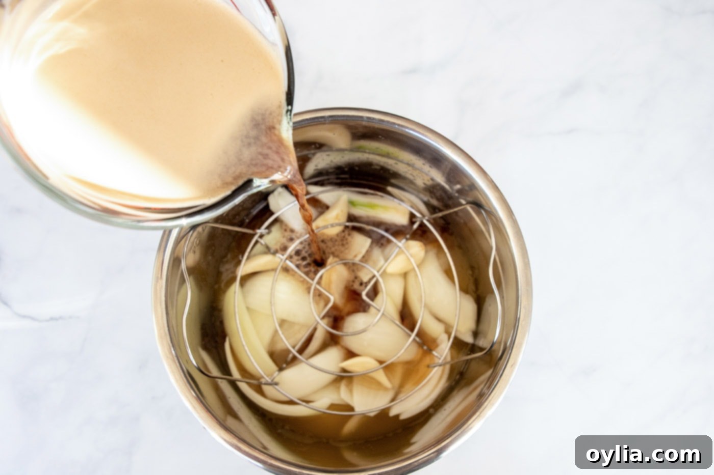 Guinness beer being poured into an Instant Pot over onion wedges and garlic cloves