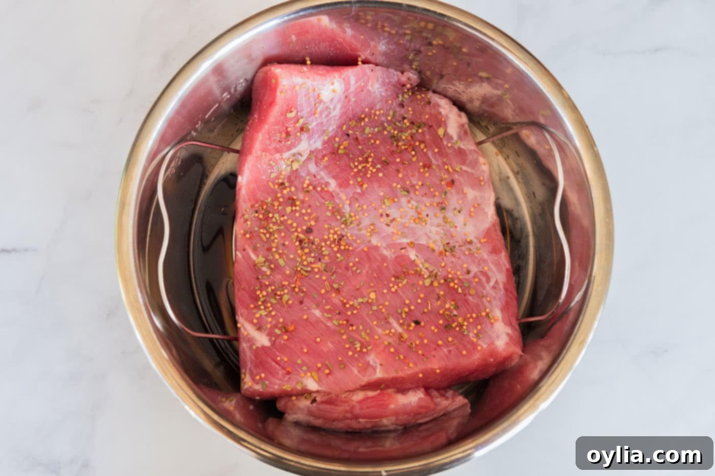 Corned beef brisket resting on a rack in an Instant Pot, generously topped with seasoning