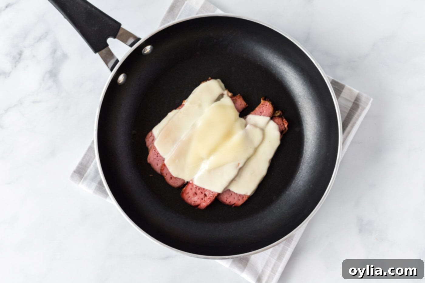 Sliced corned beef with two slices of mozzarella cheese melting on top in a hot skillet, ready to be moved to bread.