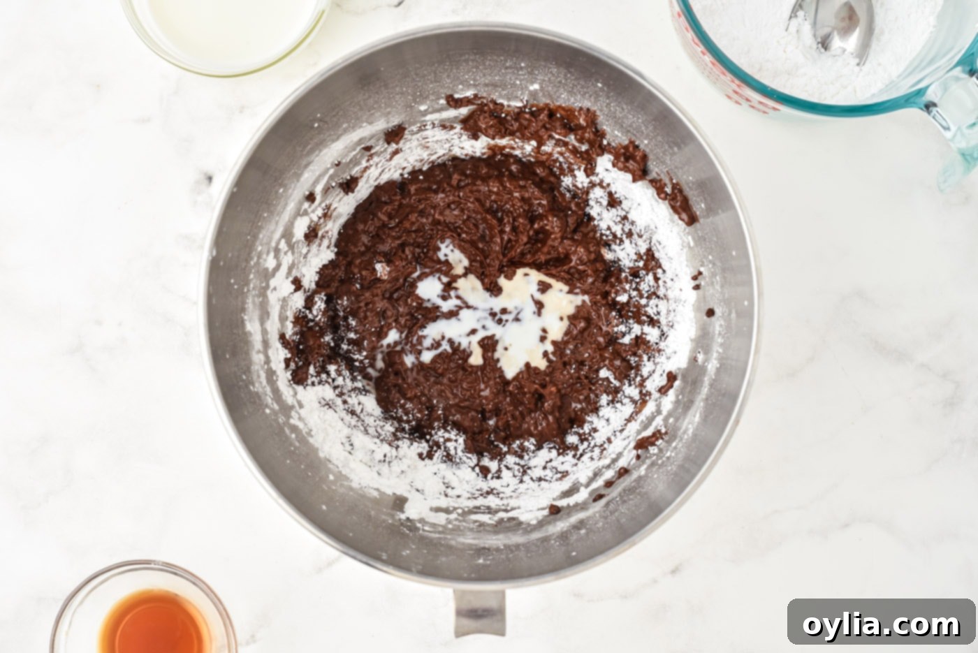 Powdered sugar and heavy cream being added to the chocolate mixture in a stand mixer.