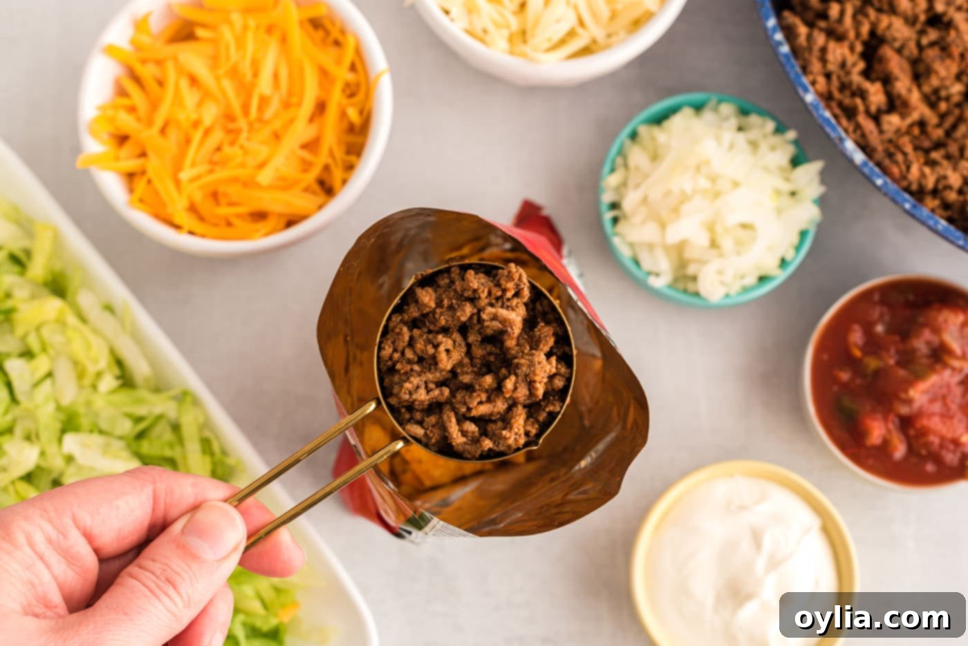 A spoon adding taco meat into an open chip bag.