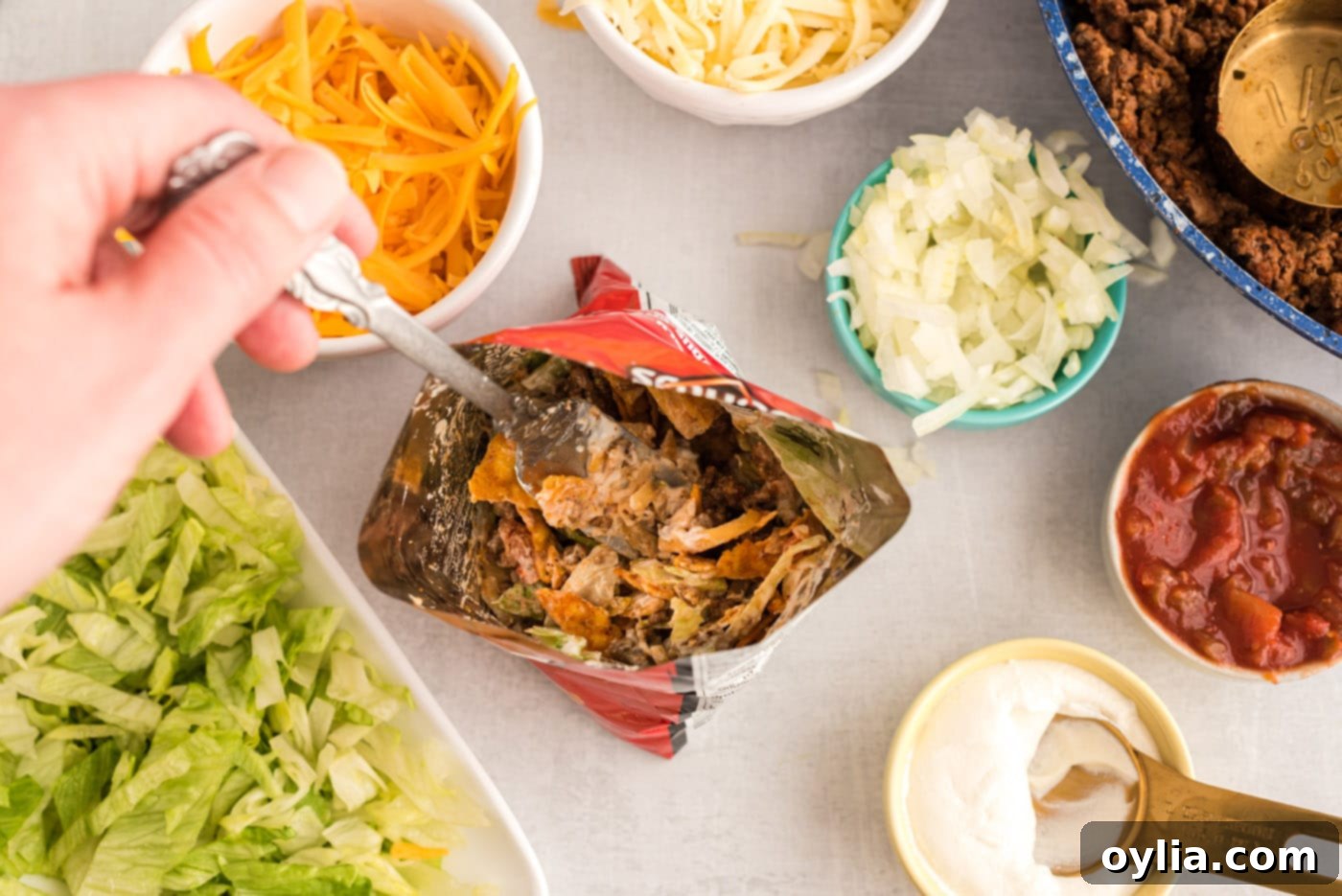 A spoon mixing taco toppings and meat into a bag of chips for a walking taco.