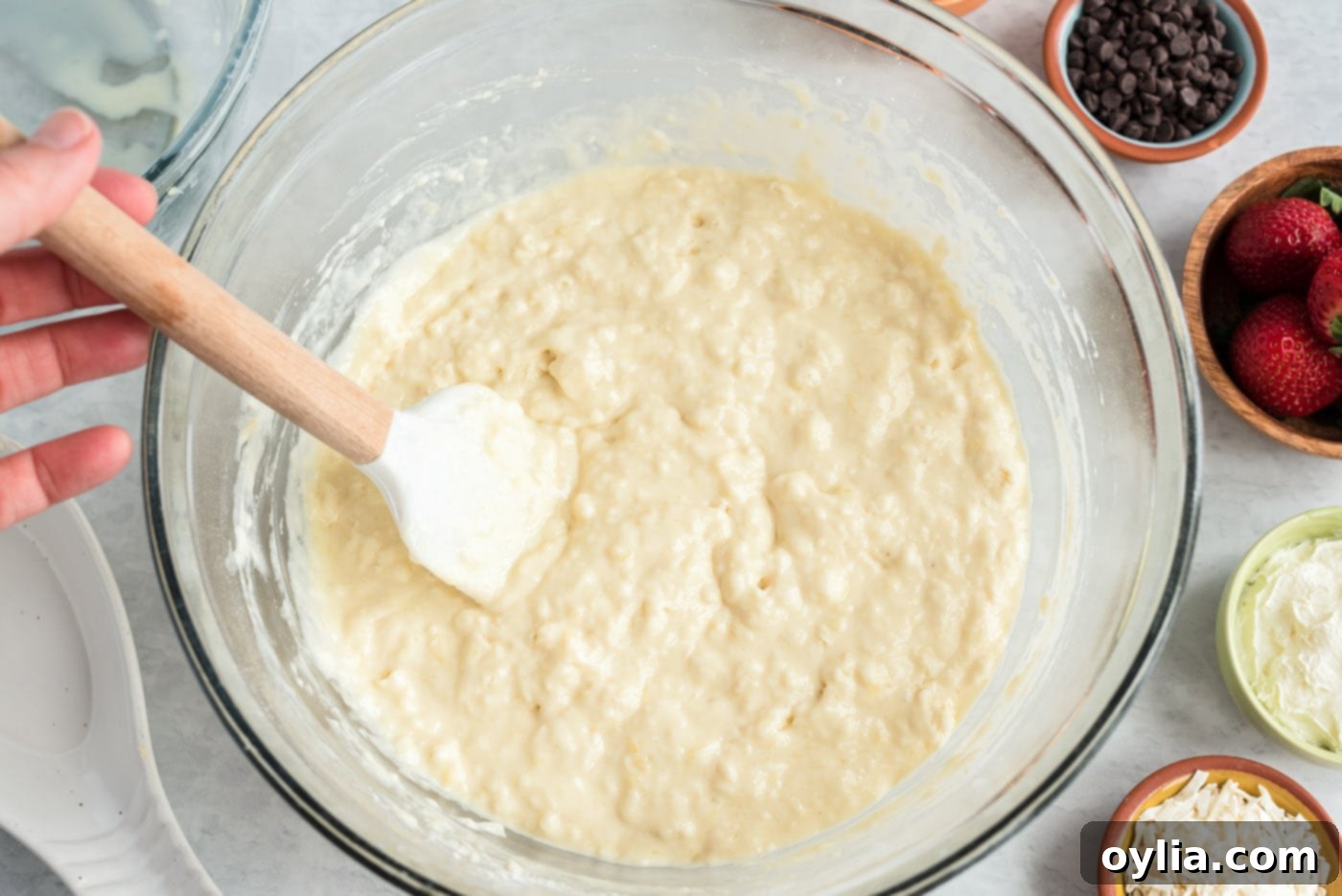 A rubber spatula gently stirring the buttermilk pancake batter, showing its slightly lumpy texture, indicating it's not overmixed.