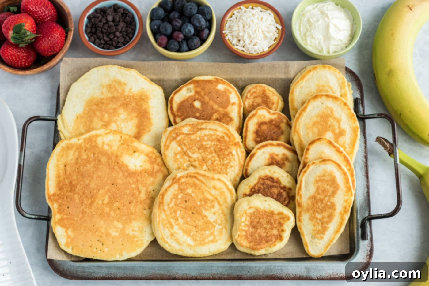 Various sizes of cooked pancakes laid out on a baking sheet, representing the different parts of the bunny: body, head, feet, and ears, ready for assembly.