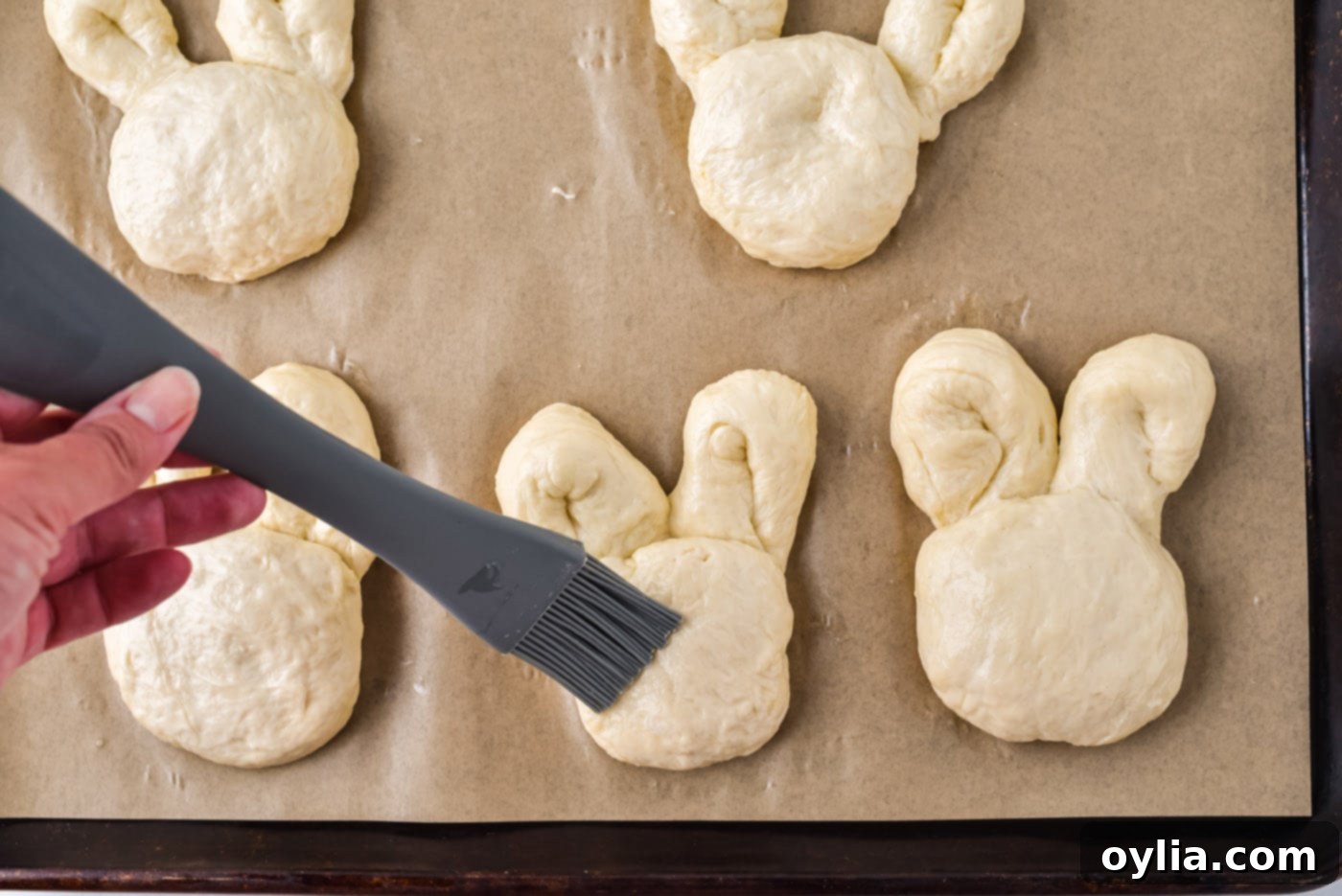 Applying egg wash to the shaped bunny rolls before baking.
