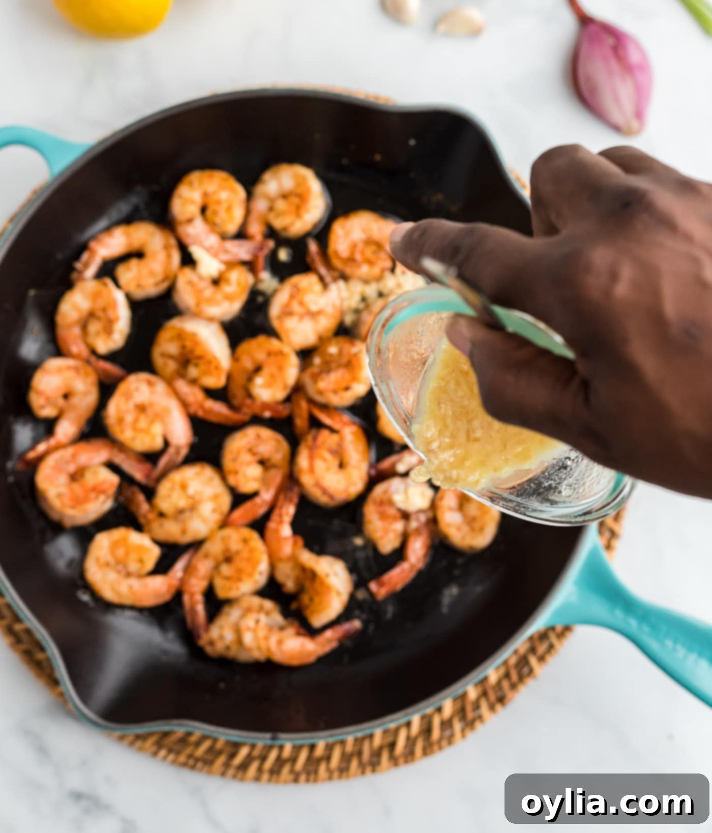 pouring butter sauce into skillet of sauteed shrimp