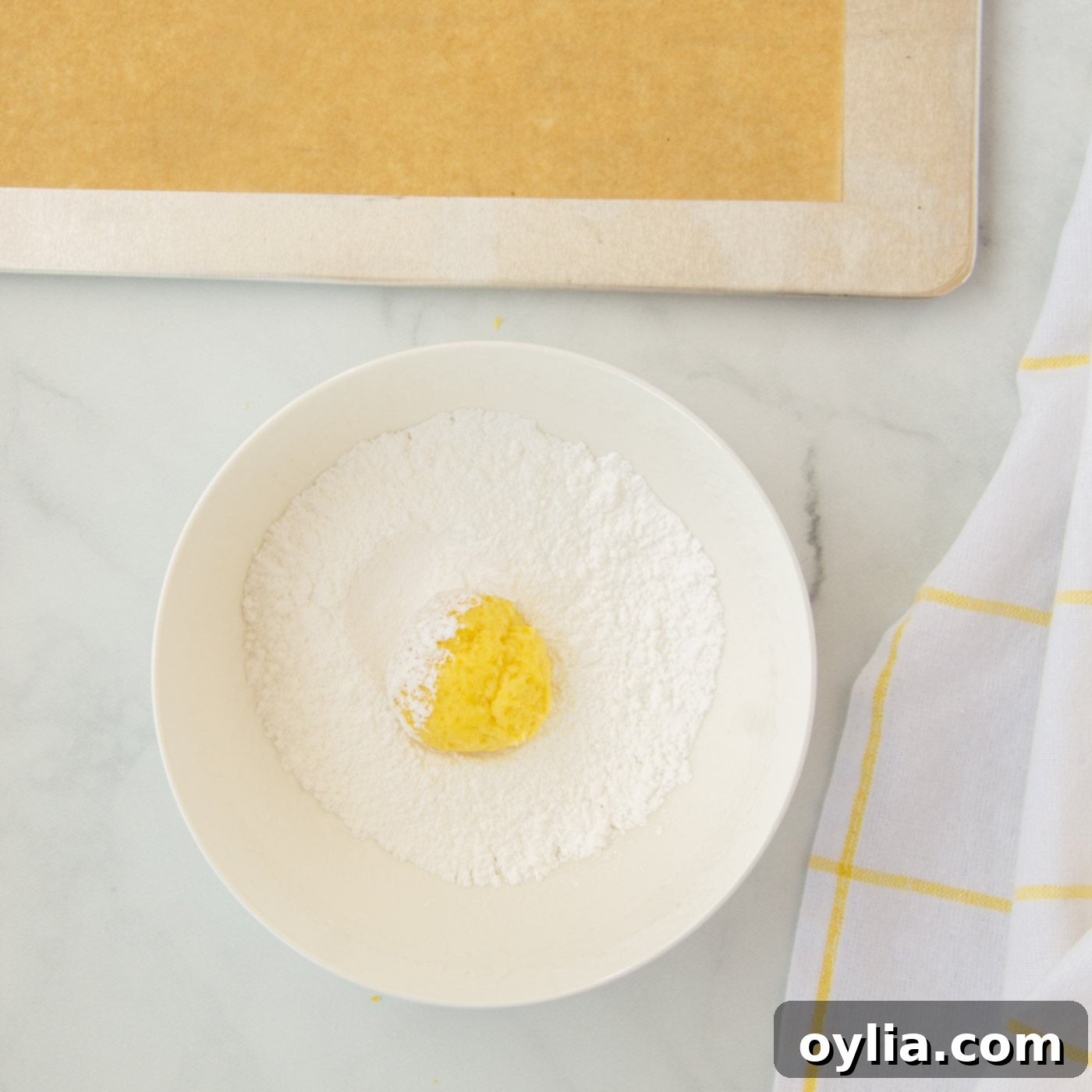 Rolling a ball of lemon cookie dough in powdered sugar to create the crinkle effect