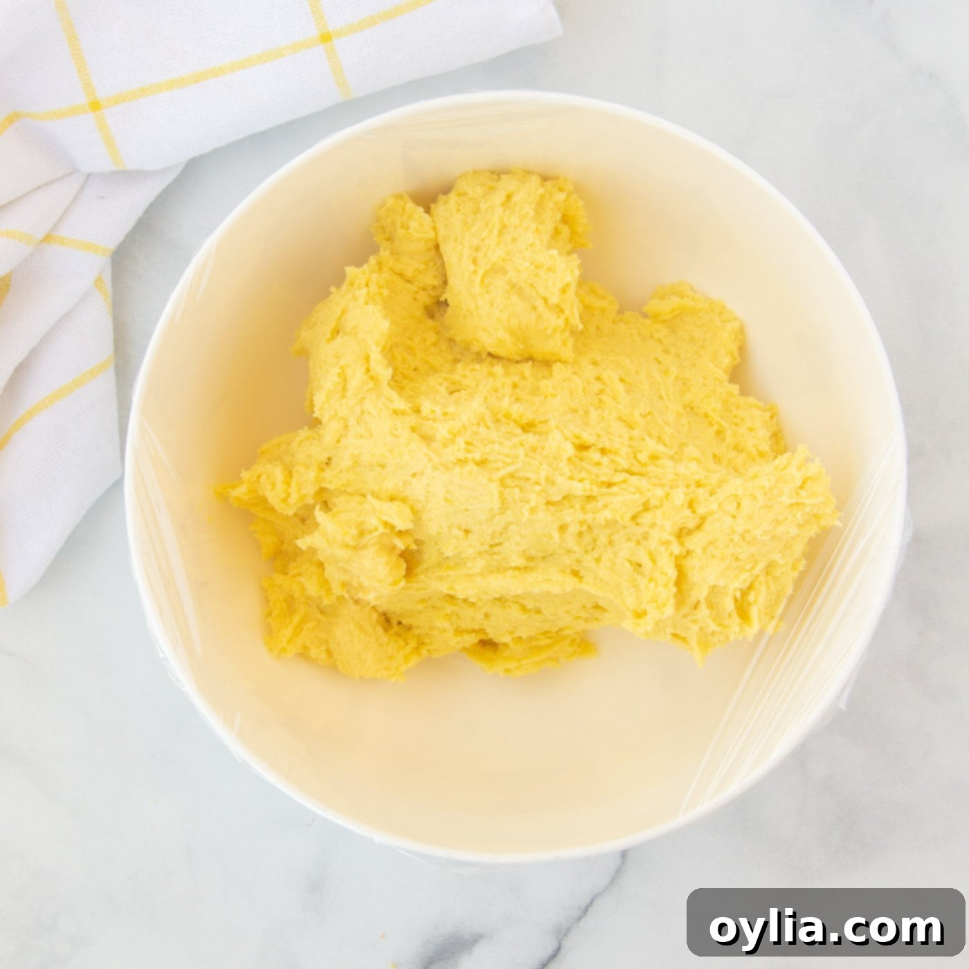 Lemon cake mix cookie dough chilling in a bowl, covered with plastic wrap