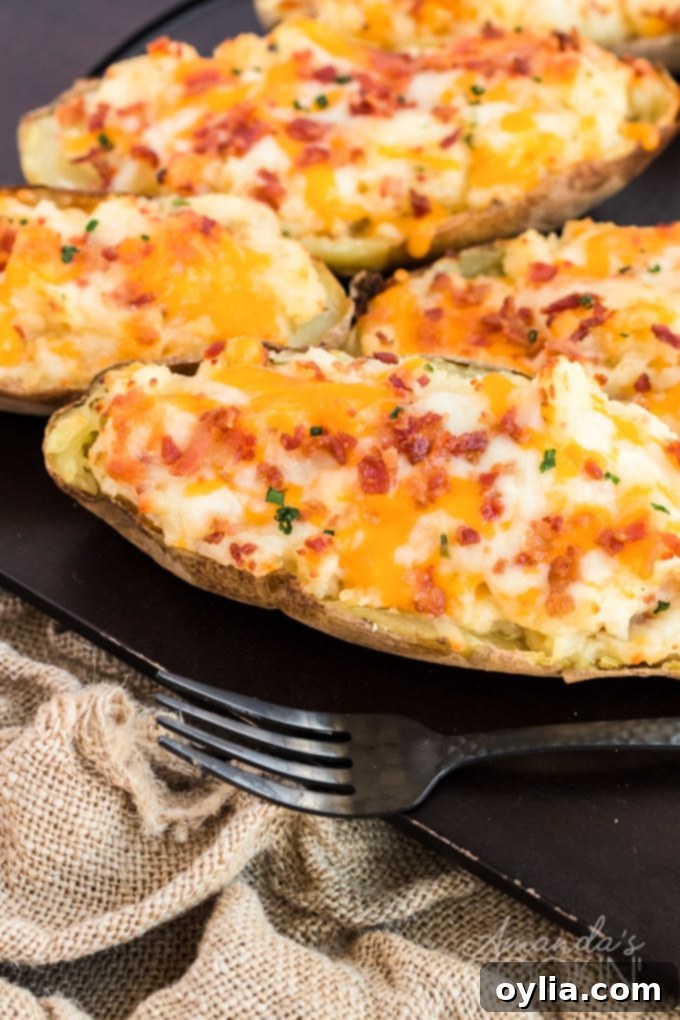 Cheesy Bacon & Chive Twice Baked Potatoes Twice baked potatoes, richly filled with cheese, bacon, and chives, presented on a dark board, ready to be served.