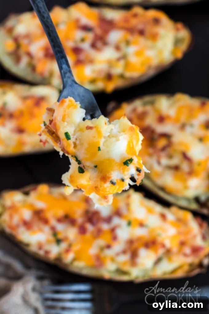 Cheesy Bacon & Chive Twice Baked Potatoes A fork piercing into a perfectly golden and fluffy twice baked potato, revealing the creamy, cheesy interior.
