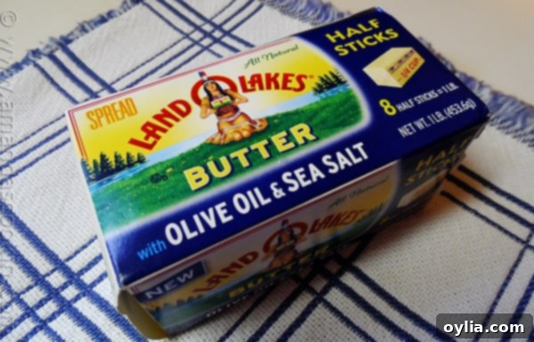 A close-up photo of the Land O' Lakes Butter with Olive Oil and Sea Salt packaging, showing its convenient stick form on a rustic wooden surface.