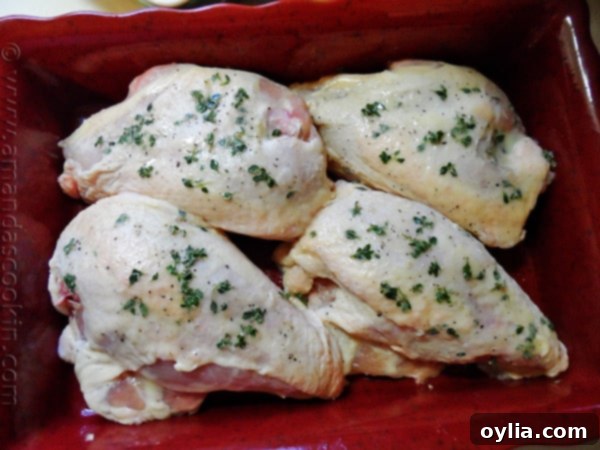 An overhead shot of raw bone-in chicken breasts in a red roasting pan, freshly brushed with the seasoned butter and adorned with vibrant green lemon thyme sprigs, just before being placed in the oven.