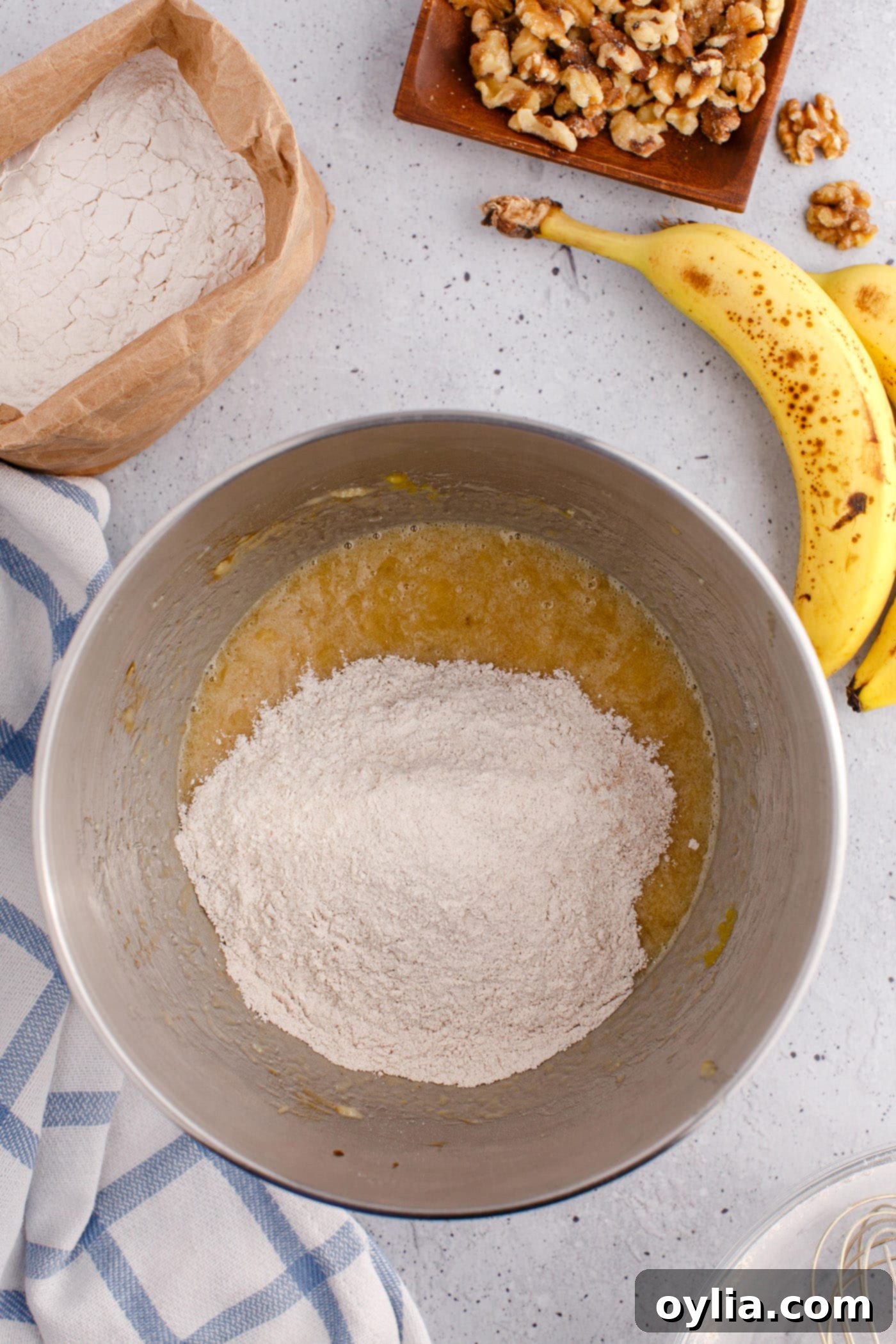 flour mixture being added to banana bread wet ingredients in a bowl