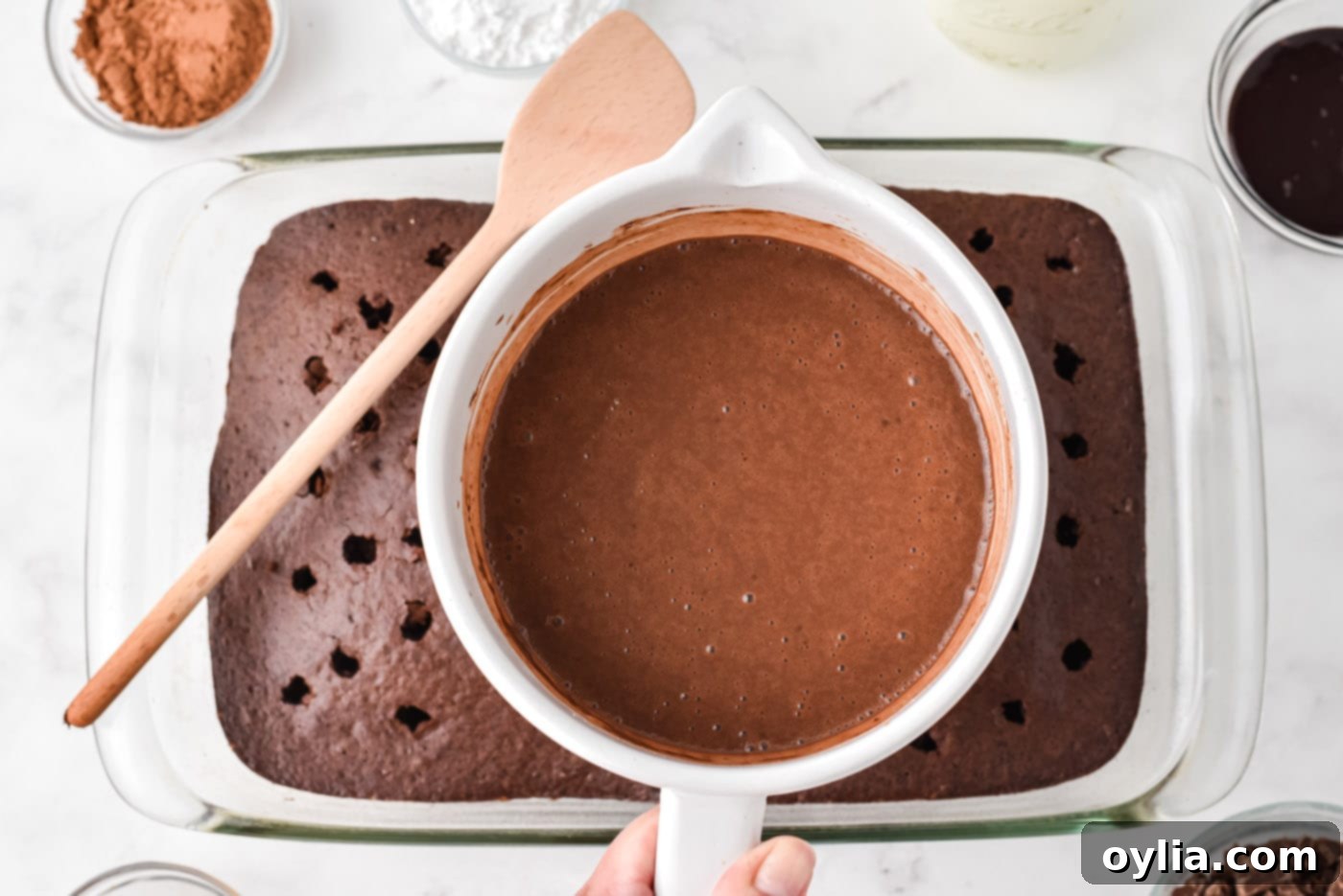 chocolate pudding being poured over the top of a poked chocolate cake, filling the holes