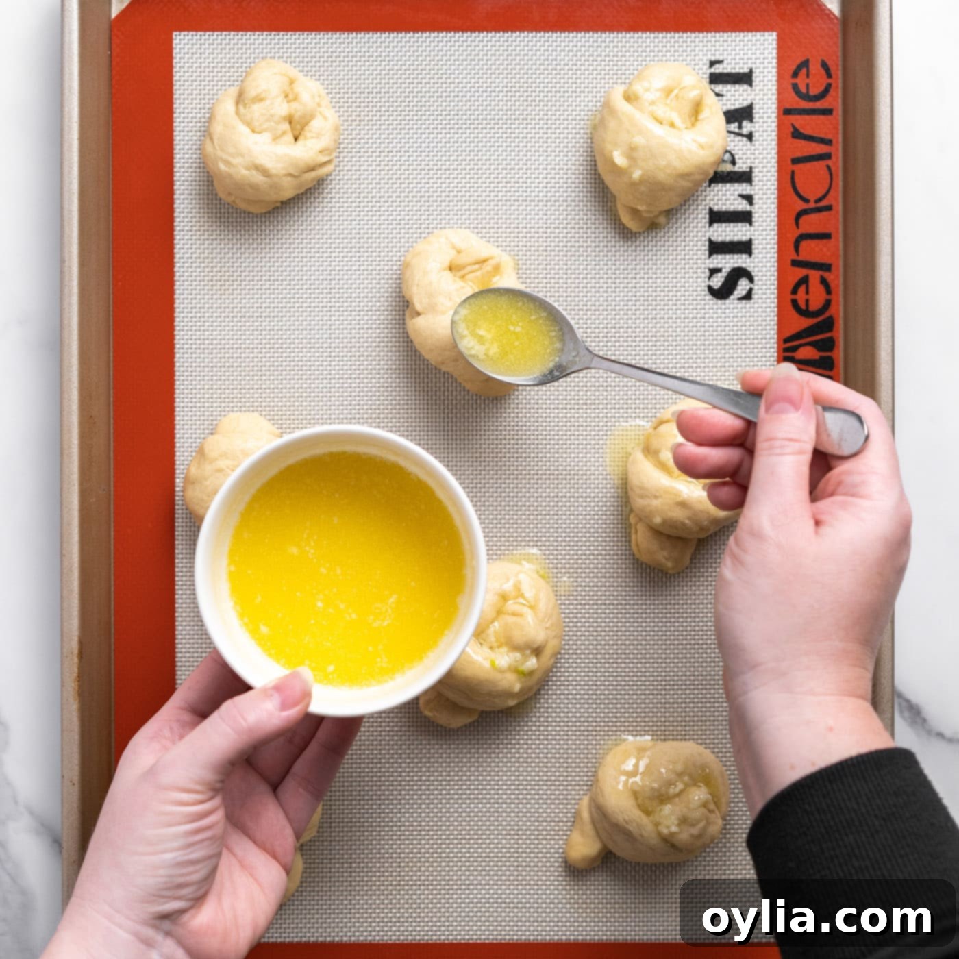 spooning garlic butter over dough knots on a baking sheet