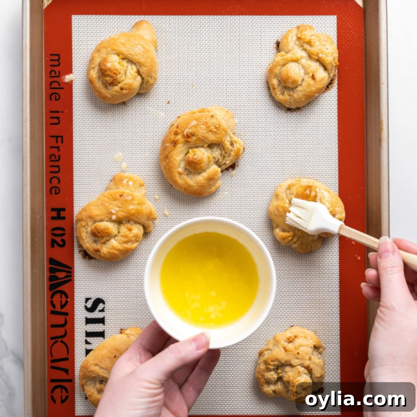 brushing extra garlic butter on top of freshly baked garlic knots