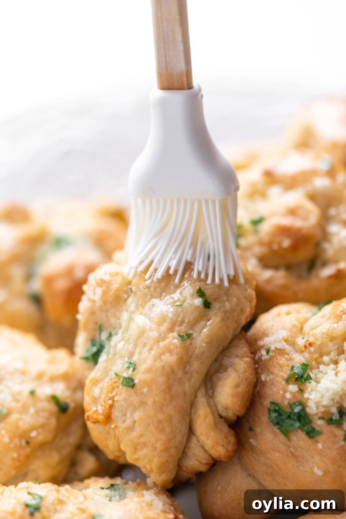 brushing garlic butter over freshly baked garlic knots