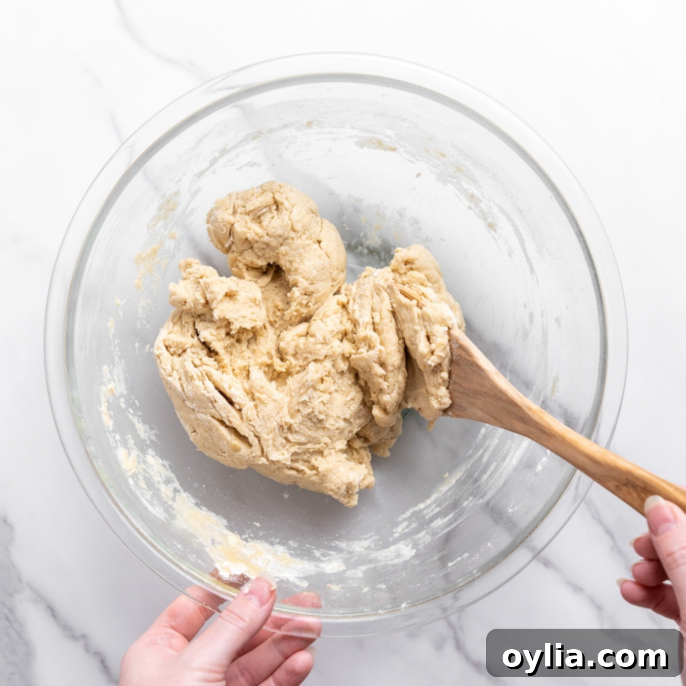 bread dough in a bowl being mixed with a wooden spoon
