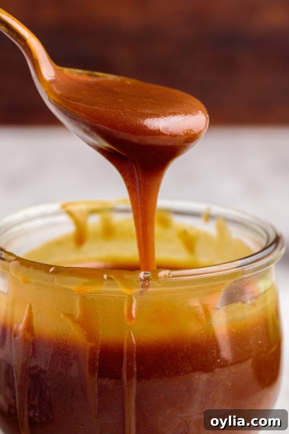 Spooning out some Caramel Sauce from a jar, showing its rich amber color and creamy texture.