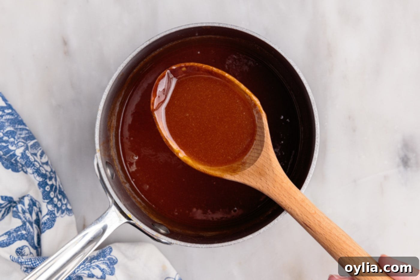 A wooden spoon holding a generous scoop of thick, amber homemade caramel sauce, ready for serving or storage.