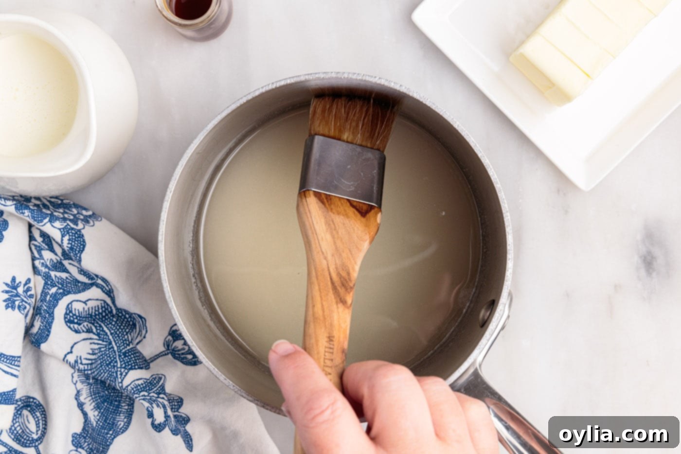 Wiping down the inside edges of the saucepan with a wet pastry brush to prevent sugar crystallization.