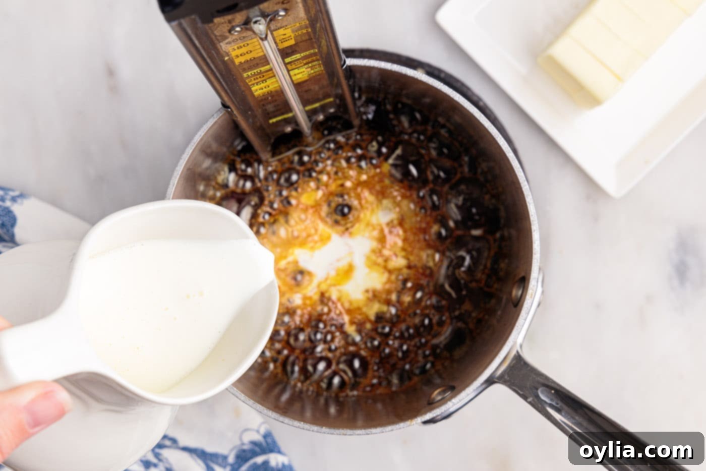 Heavy cream being slowly poured into hot caramel sauce, causing it to bubble and thicken.
