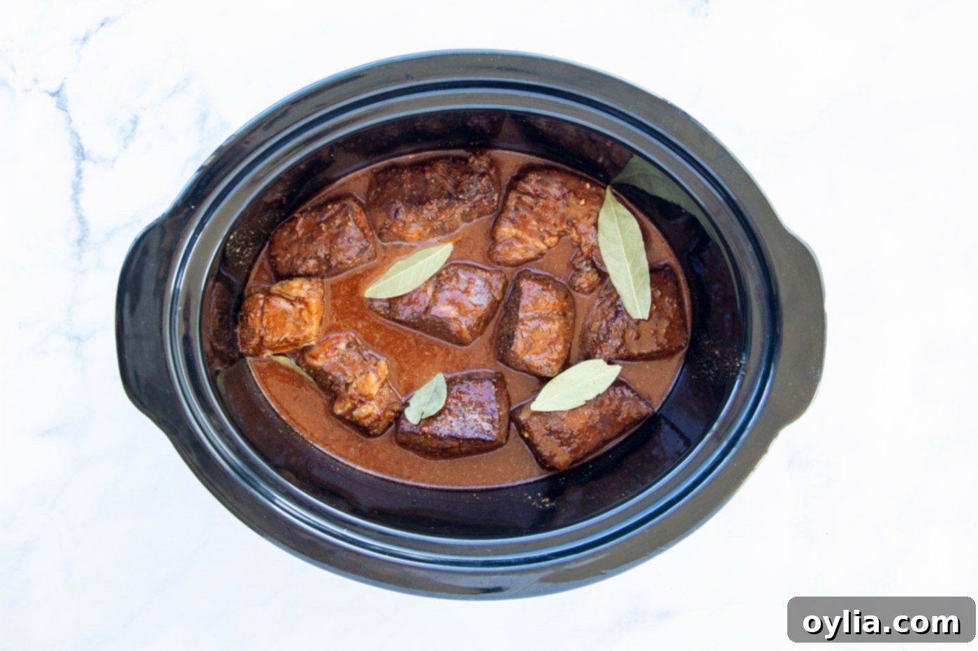 Beef barbacoa simmering in the crockpot, covered with the flavorful seasoning mixture and bay leaves