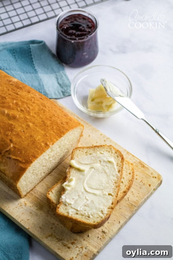 An overhead view of a golden-brown homemade white bread loaf with a slice buttered and ready to eat.