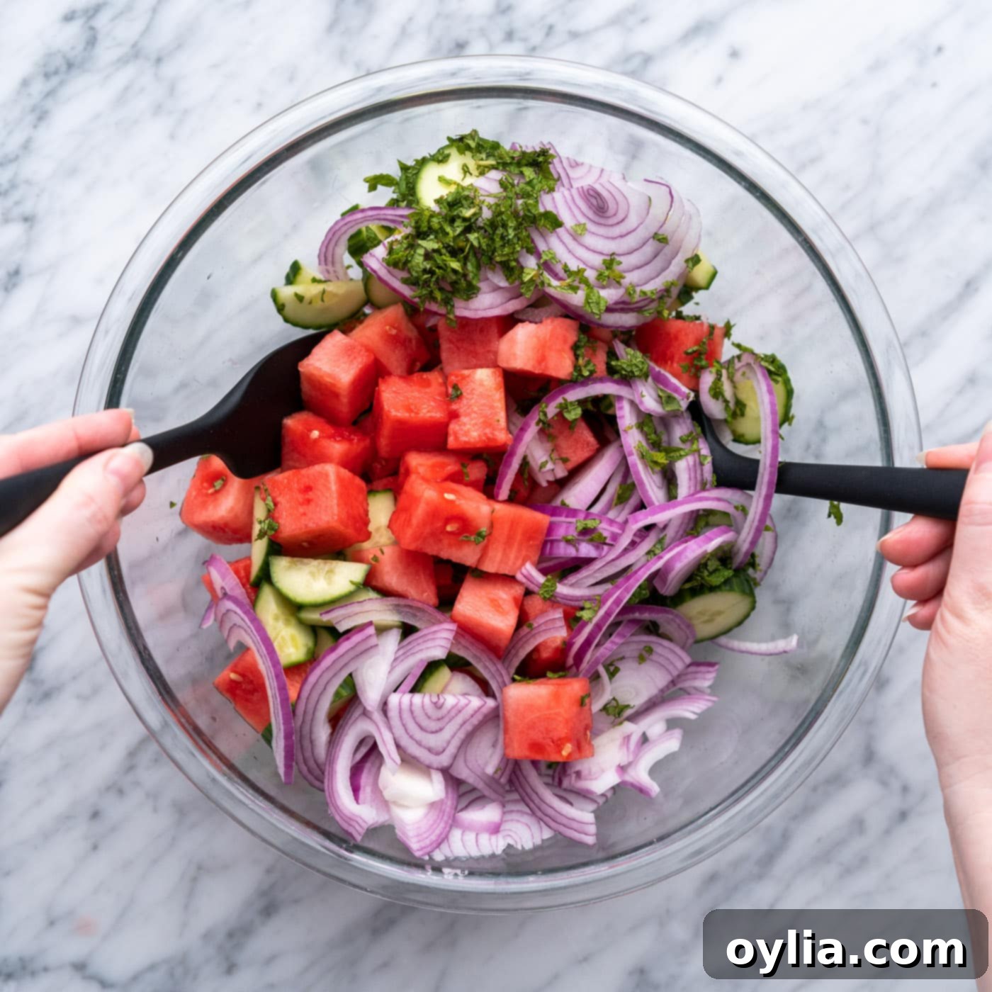 tossing watermelon salad ingredients together in a bowl