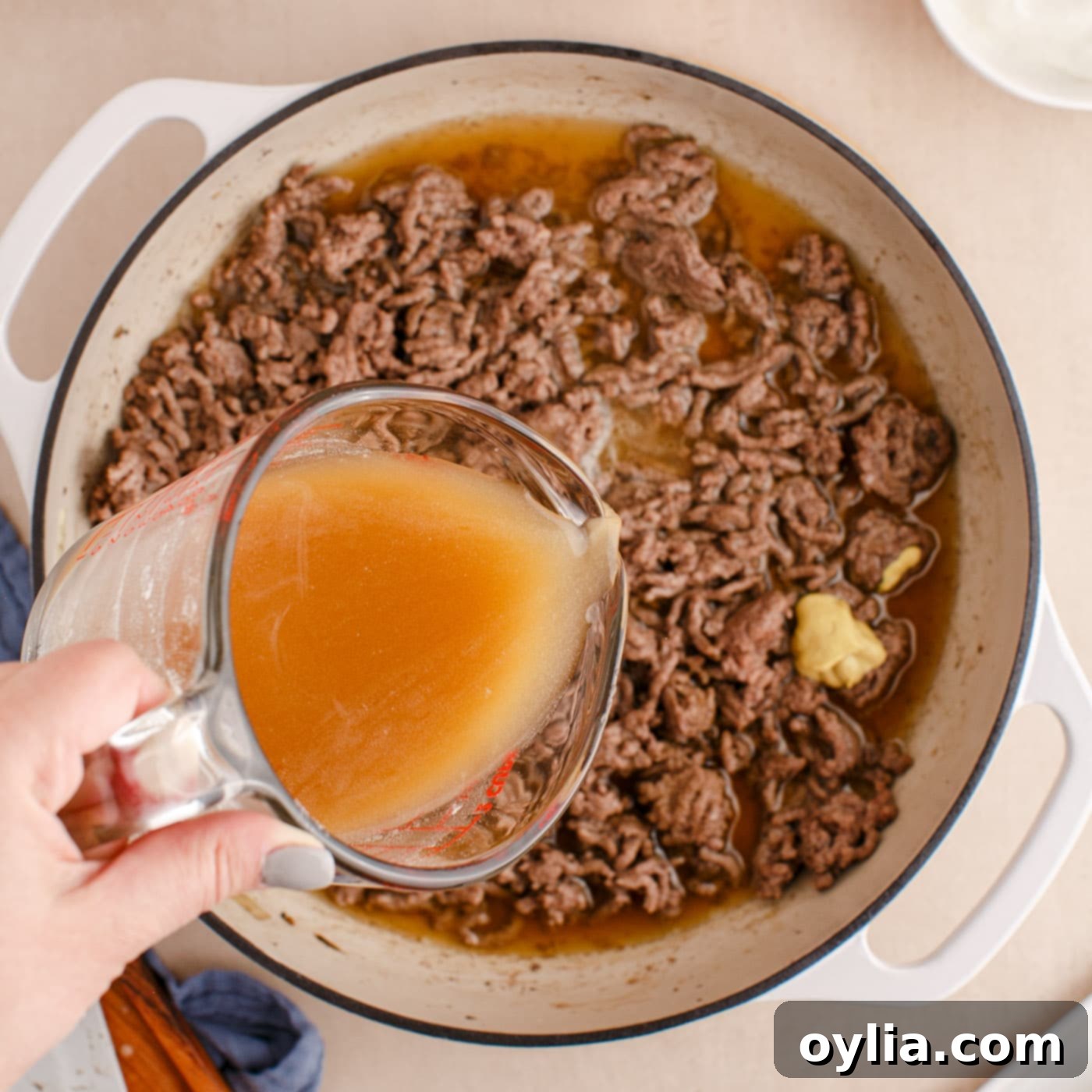 adding beef broth and flour mixture to ground beef in a skillet