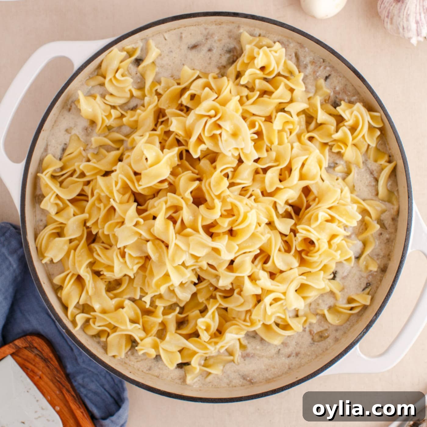 cooked egg noodles added over ground beef stroganoff in a skillet