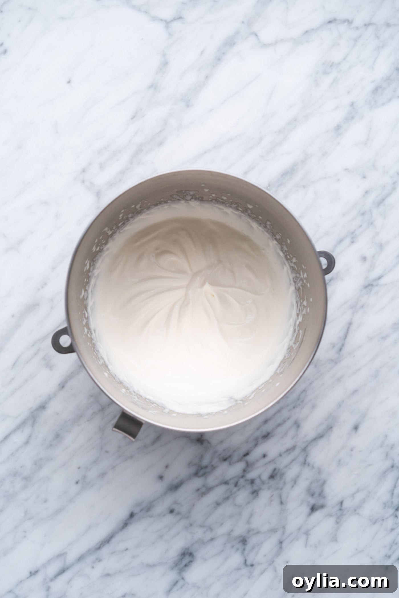 Whipped cream forming soft peaks in a mixing bowl before gelatin is added