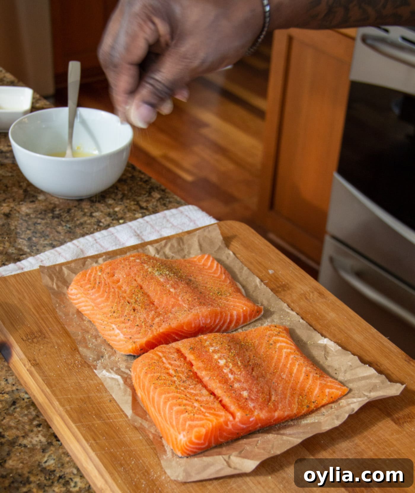 Sprinkling lemon pepper and garlic salt onto salmon fillets on a cutting board, preparing them for the marinade.