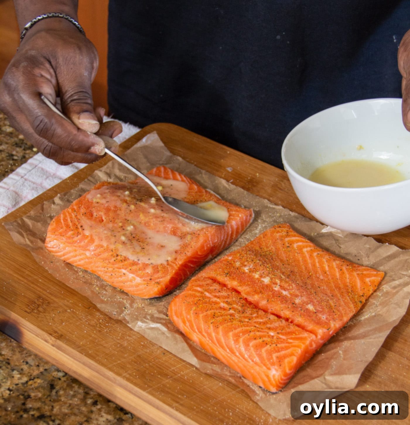 Spoonfuls of rich lemon marinade being drizzled over seasoned salmon fillets, infusing them with flavor.
