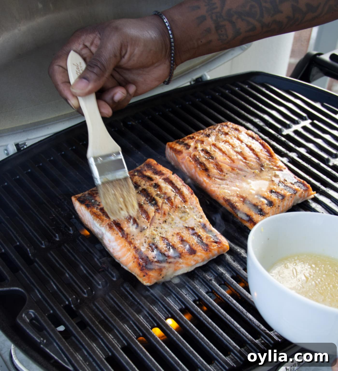 A chef brushing lemon marinade onto salmon fillets as they cook on a hot grill, enhancing their flavor and moisture.
