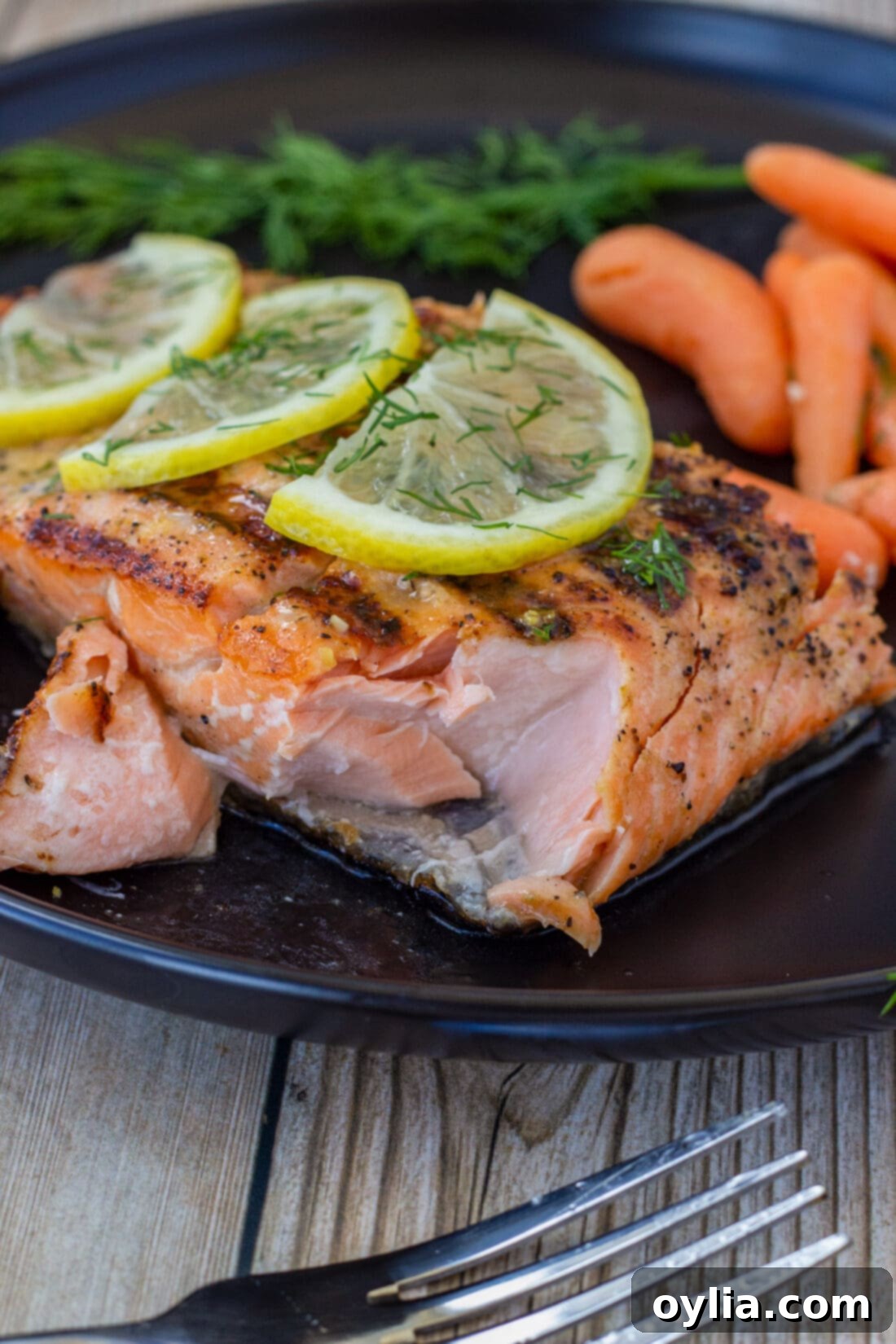 A close-up of a grilled lemon salmon fillet with a bite taken out, revealing its flaky, tender interior.