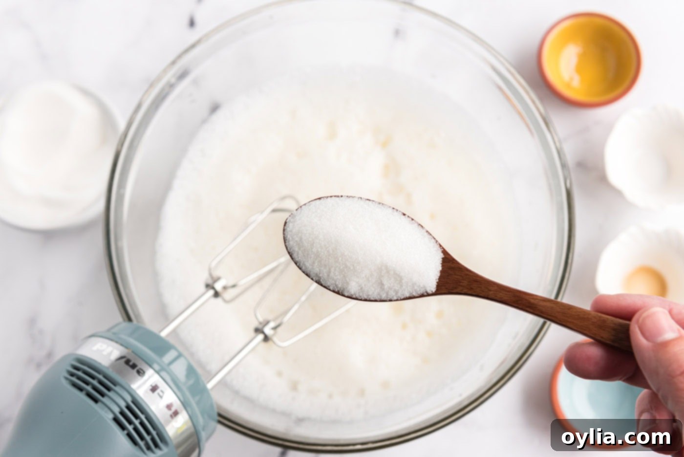 spooning granulated sugar into bowl of egg white mixture during whipping