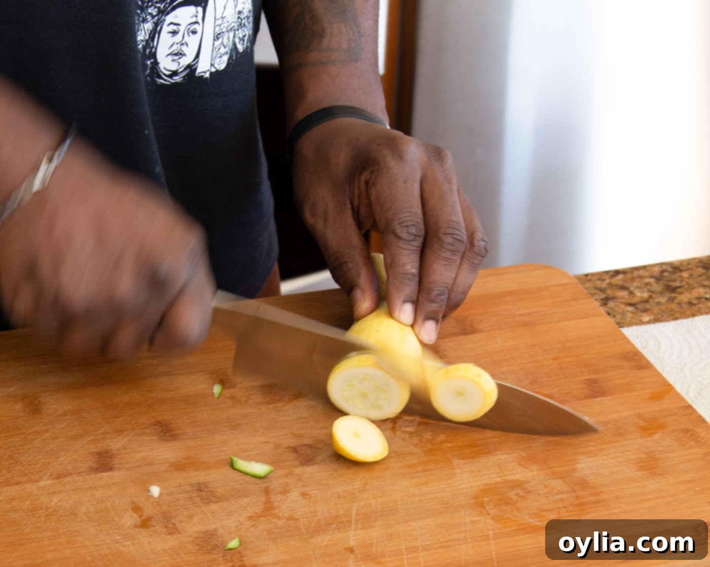 A hand cutting yellow squash into even pieces for shrimp kabobs.